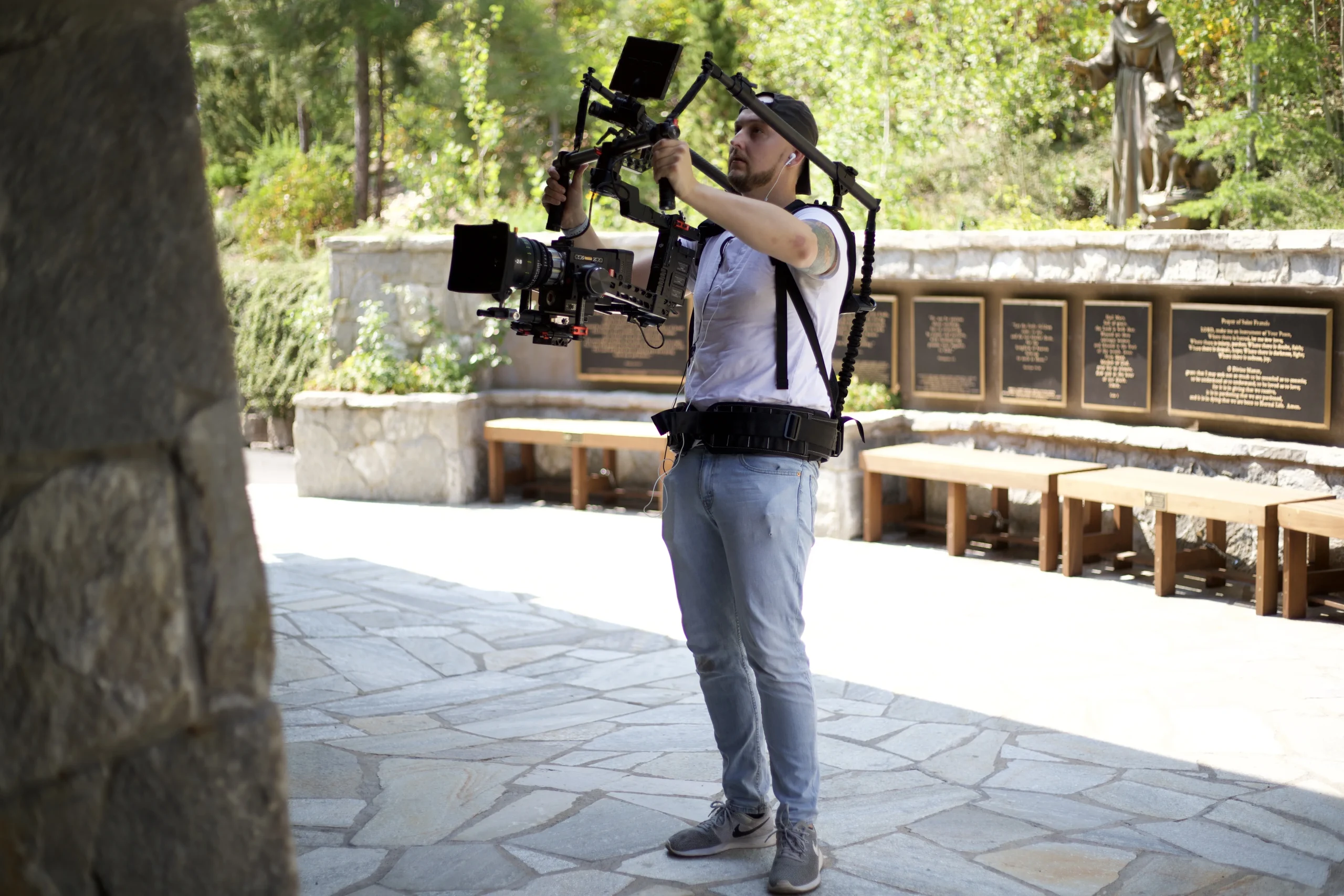 A Sunday to Sunday camera operator filming beside a statue of St. Francis